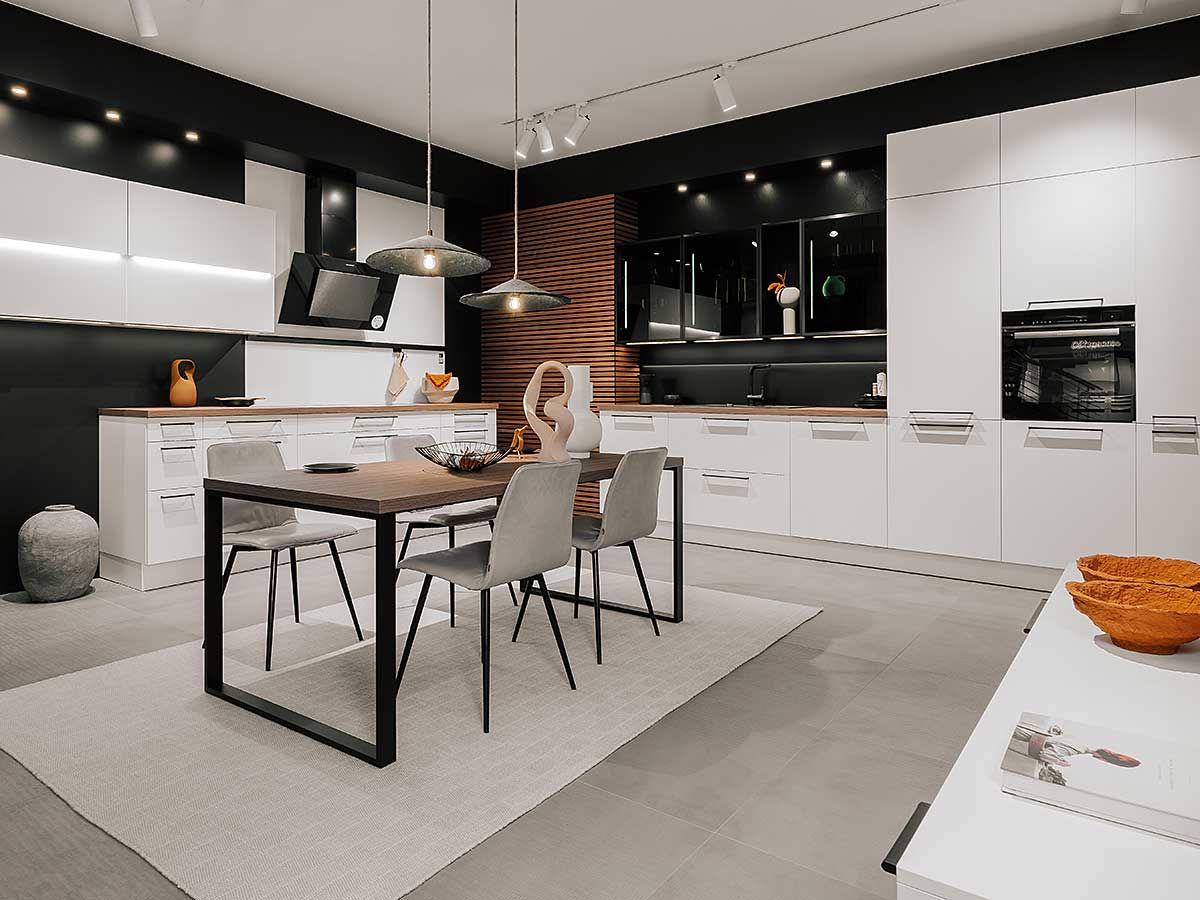 Eine große, weiße Küche mit Esstisch aus Holz in der Mitte und schwarzen Wänden mit Holzakzenten