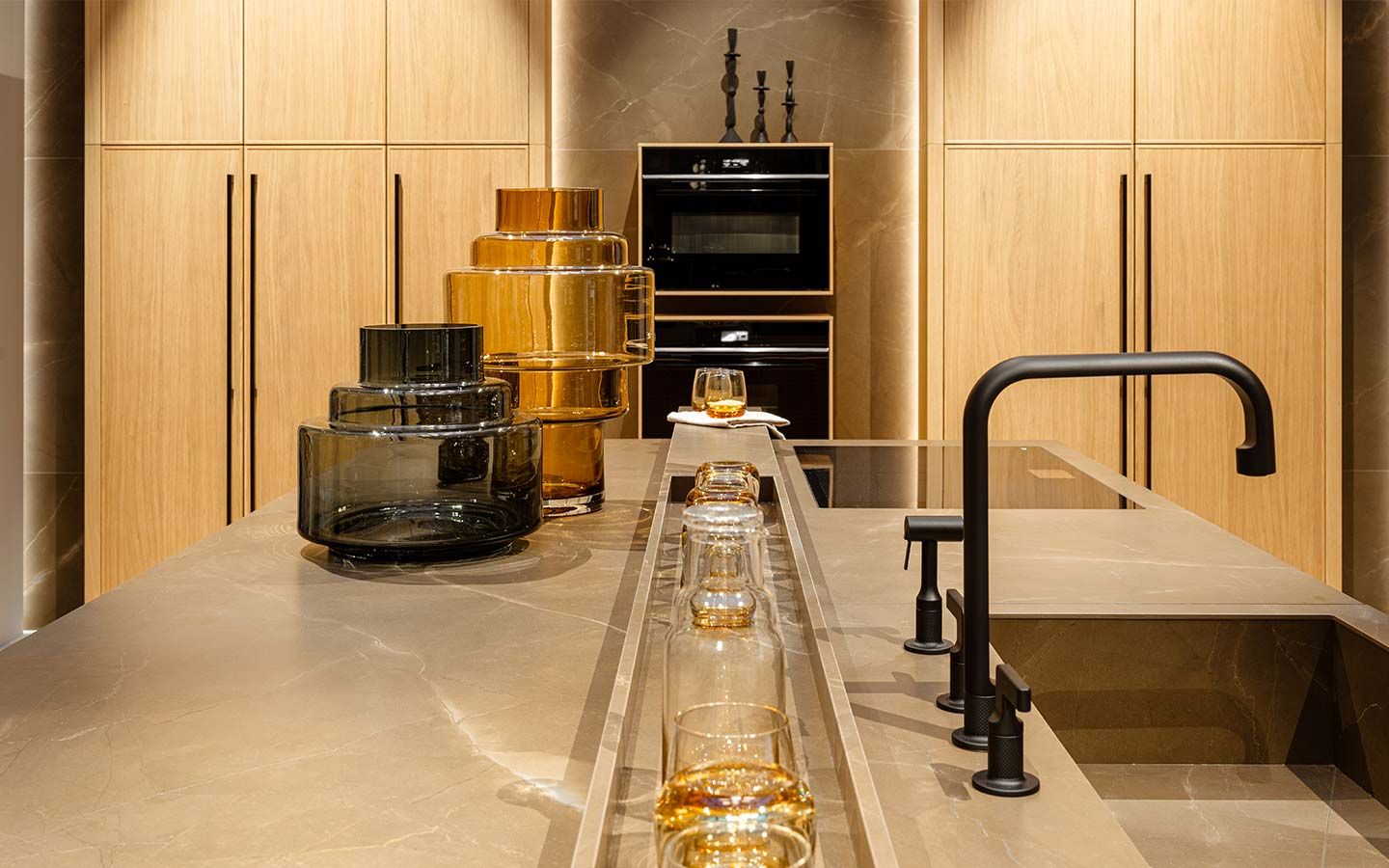 Helle Küche mit Dekorativen Gläsern EIne Helle Küche mit Holzschränken und steinender Arbeitsplatte mit schwarzen Armaturen und dekorativen Gläsern