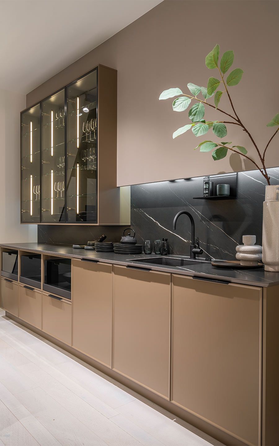 Dunkelbeige Küche mit Pflante Eine dunkelbeige Küchenfront mit großer weißer Vase in der eine Pflanze ist