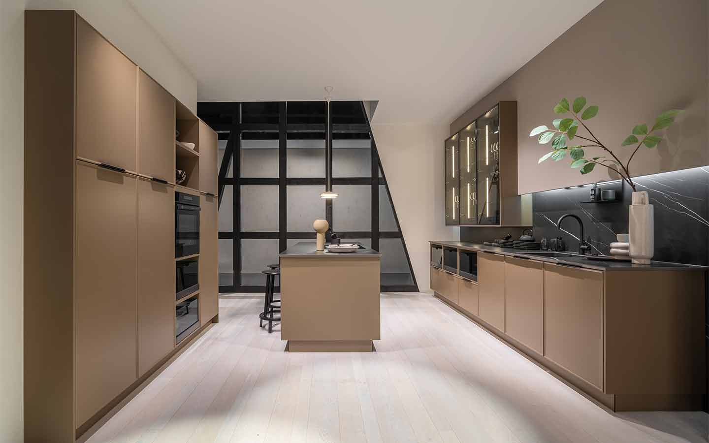 Braune Küche mit Fensterfront Eine braune Küche mit Kochinsel vor einer Fensterfront mit breiten Fensterumrandungen