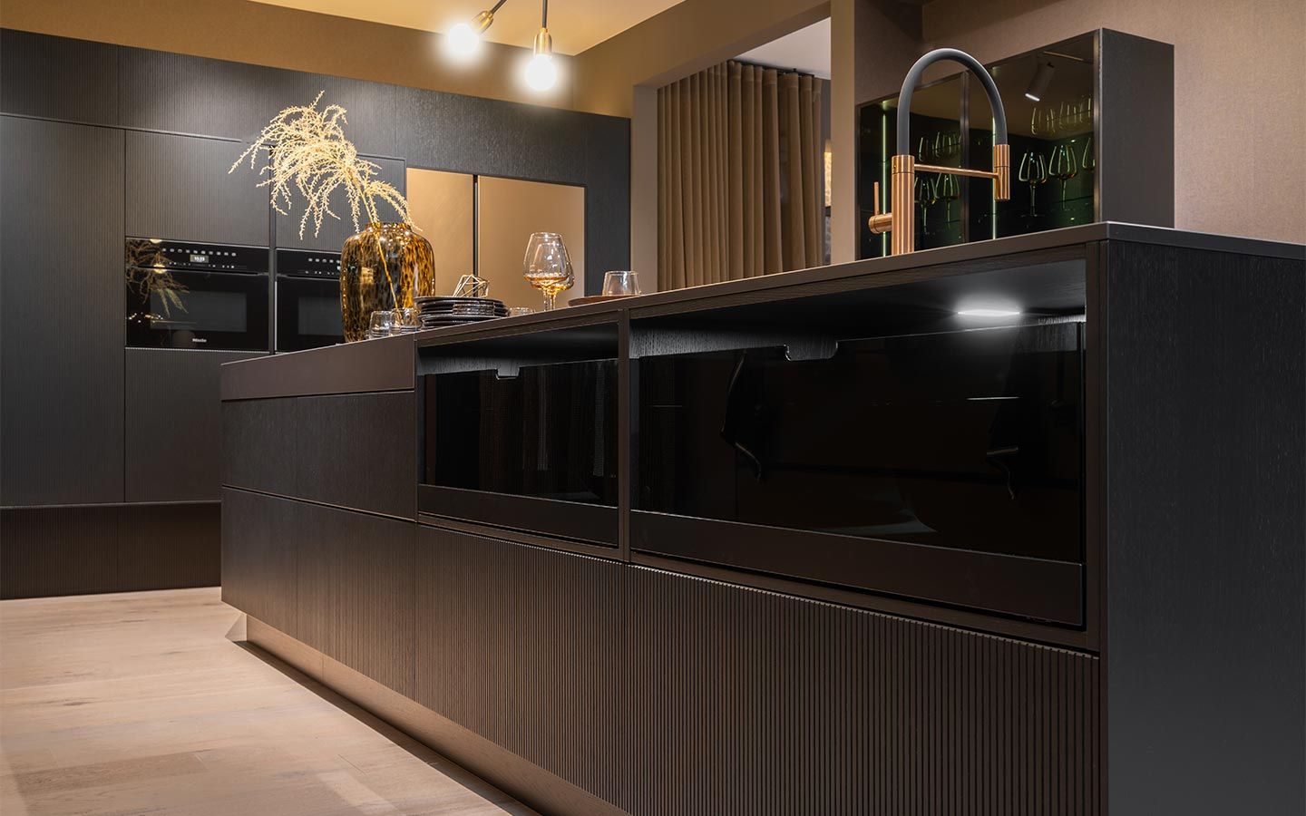 Dunkle Kochinsel mit goldenen Wasserhahn Eine Dunkle Kochinsel mit offenen Schubladen aus getöntem Glas und goldenem Wasserhahn