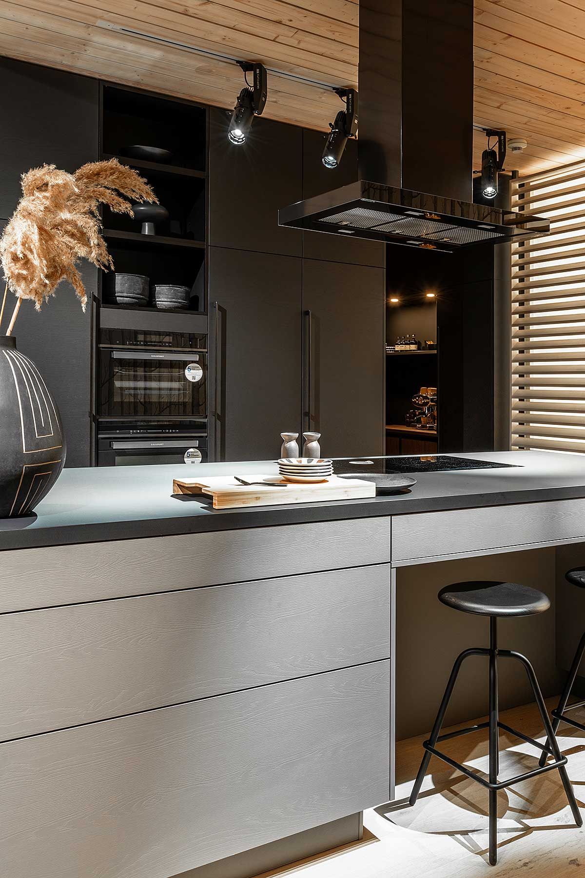 Eine Küche mit schwarzen Schränken und einer Weiß verkleideten Kochinsel mit schwarzglänzenden Rauchabzug