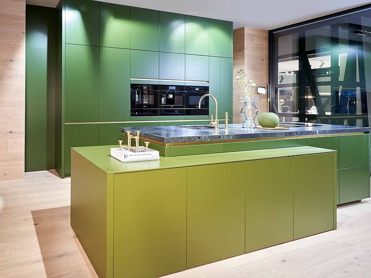 Eine Küche mit mehreren Grüntönen und einer Marmor Arbeitsplatte mit großem Fenster