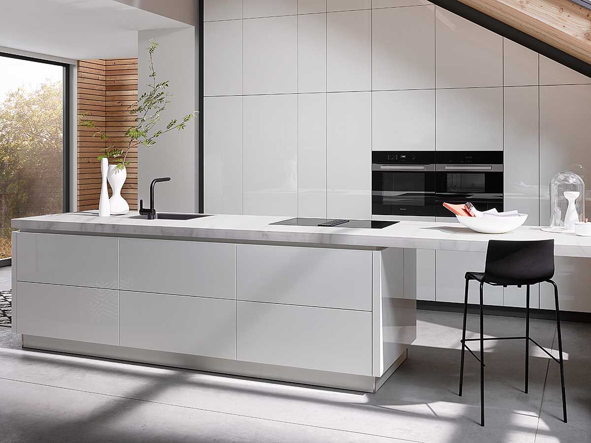 Eine weiße Küche mit Insel und einem eingebauten Backofen unter einer Dachschräge mit Dachfenster